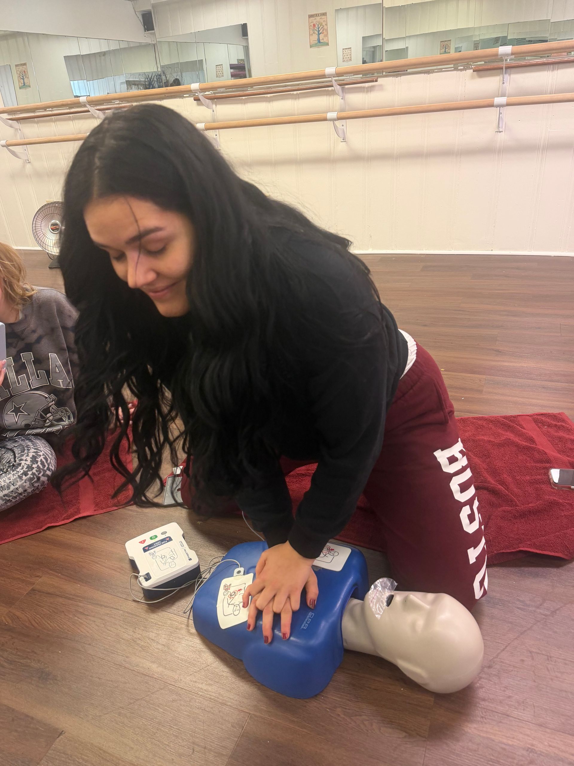 Woman practicing CPR on a training dummy, using an AED, in a classroom setting.