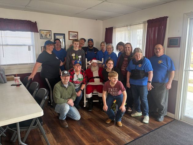 A group of people gathers in a room with a person dressed as Santa Claus, posed for a photo.