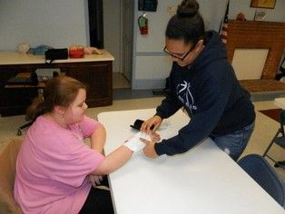 A woman is putting a bandage on another woman 's arm.