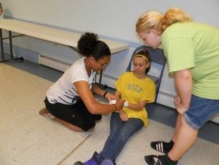 A girl in a yellow shirt is getting a bandage on her leg