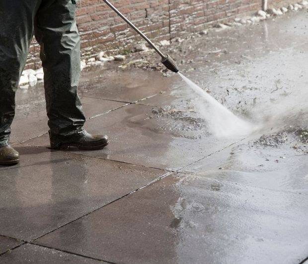 A man is using a high pressure washer to clean a sidewalk.