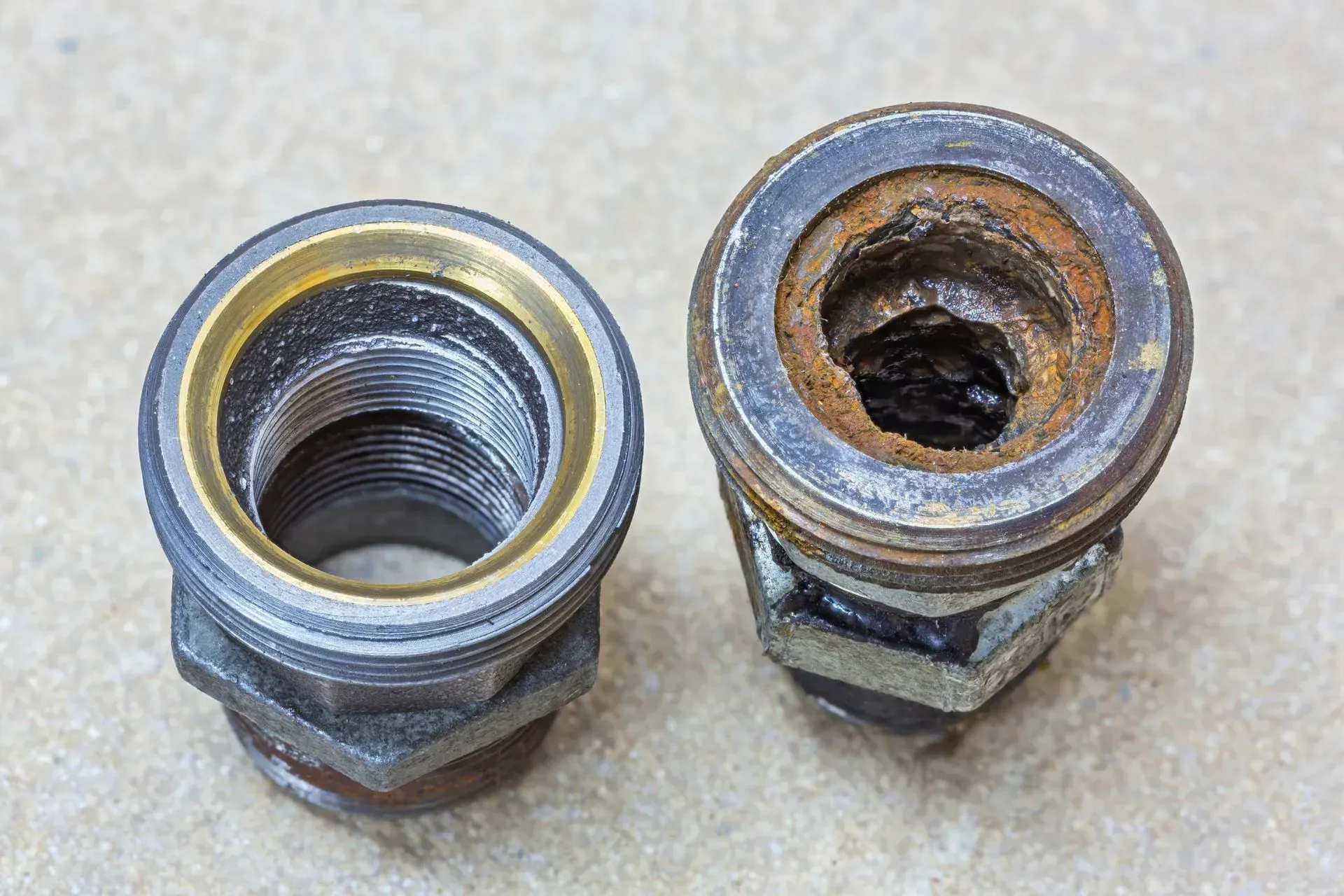 Two metal pipe fittings, one clean, the other heavily corroded with rust.