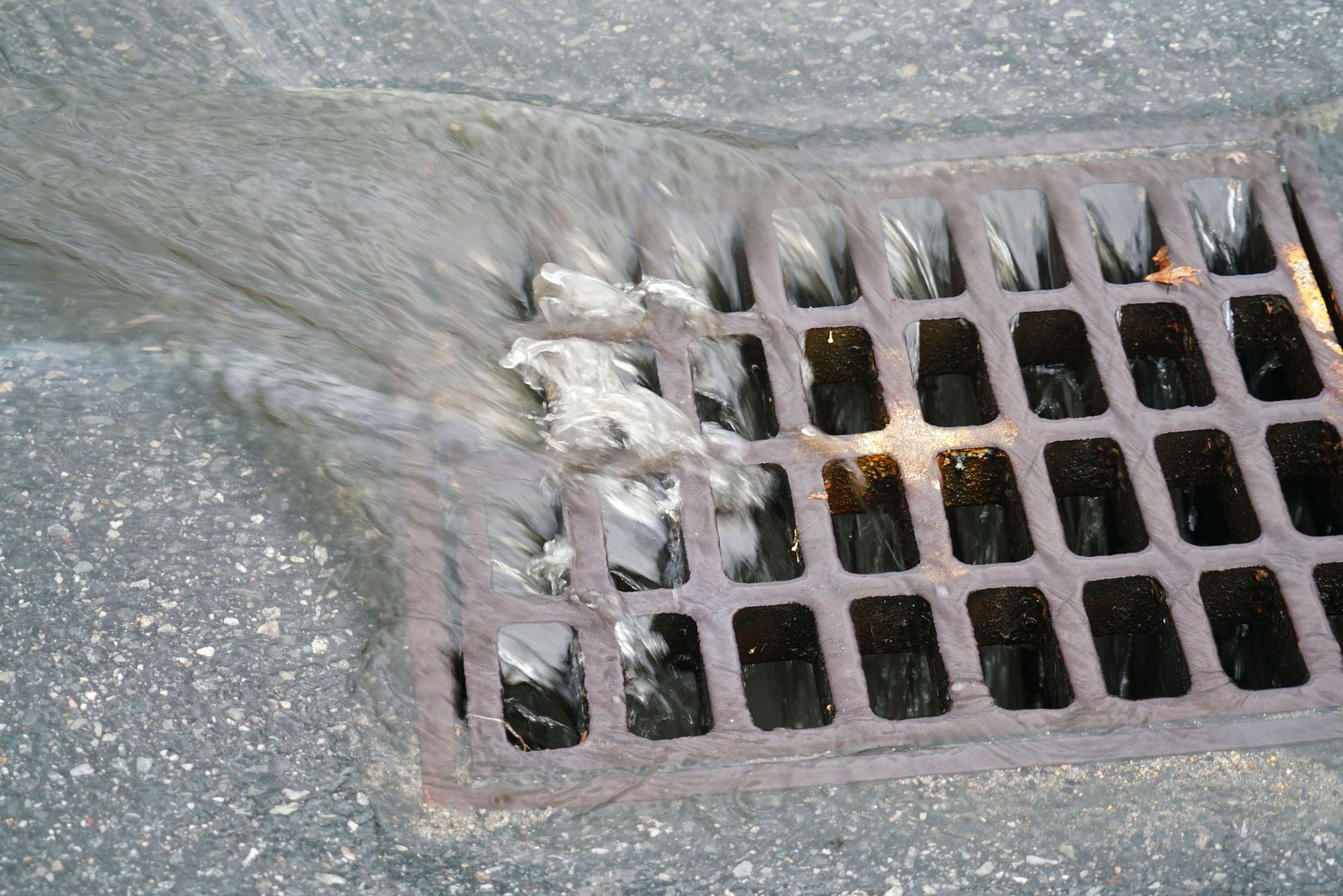 Water flowing over a metal storm drain on asphalt.