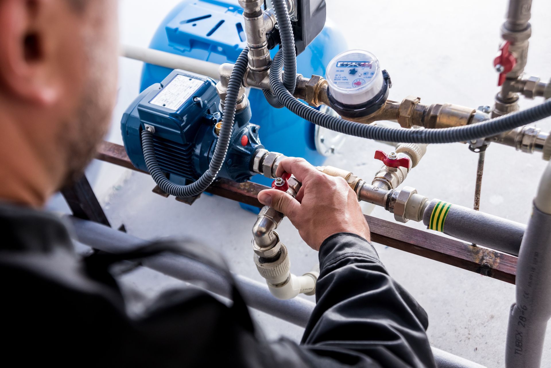 Person adjusting a red valve on a water pump system, outdoors.