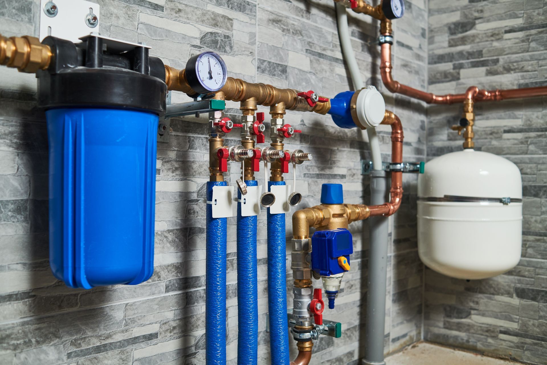 Plumbing system with blue filter, copper pipes, and pressure gauges against tiled wall.