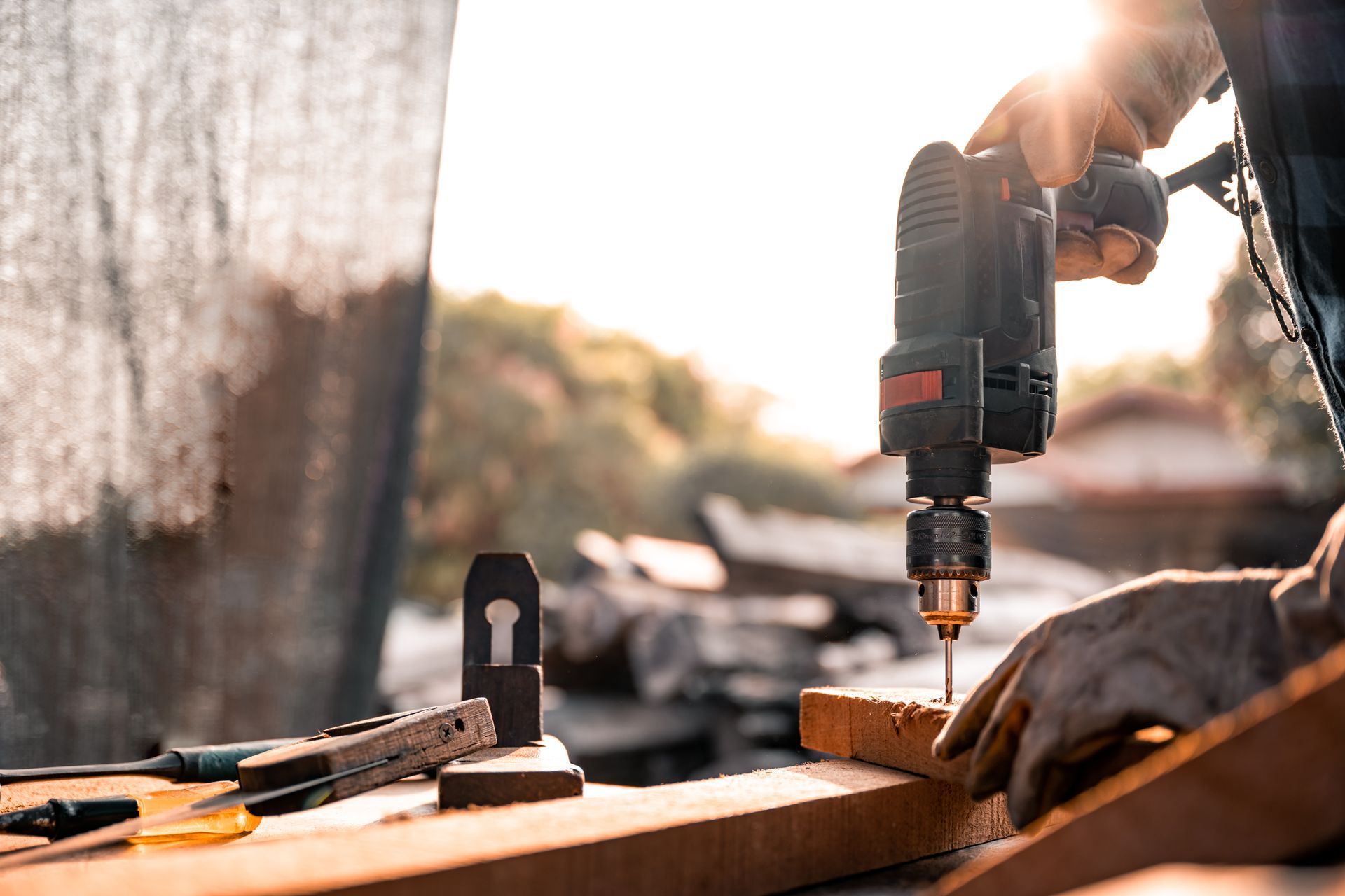 Carpenter using a drill on a wooden plank at a construction site, sunlight in background.