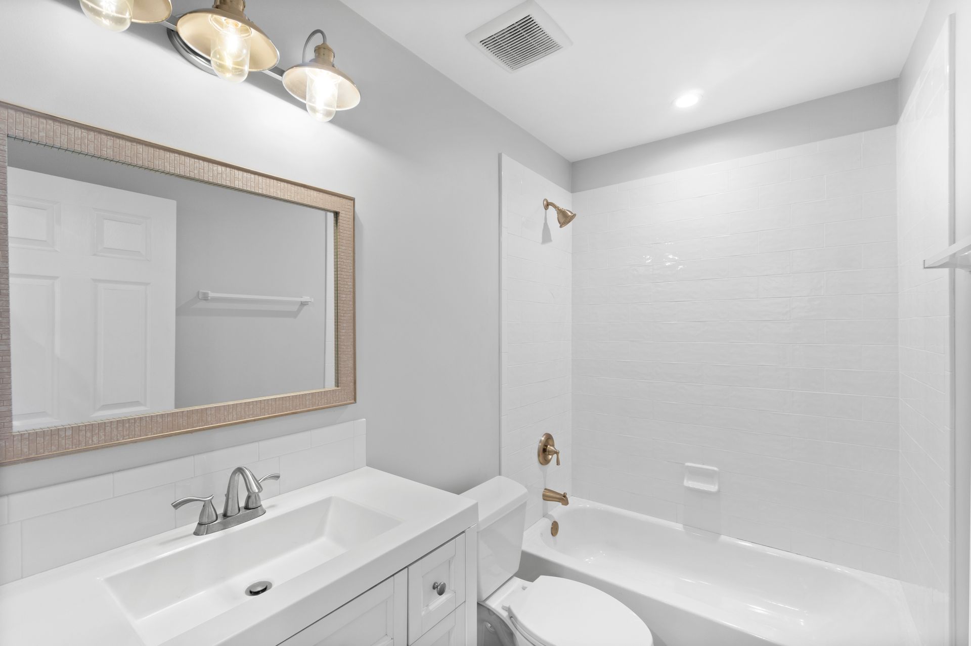 Bathroom with white walls, a sink, toilet, and bathtub. The mirror has a light-colored wooden frame.