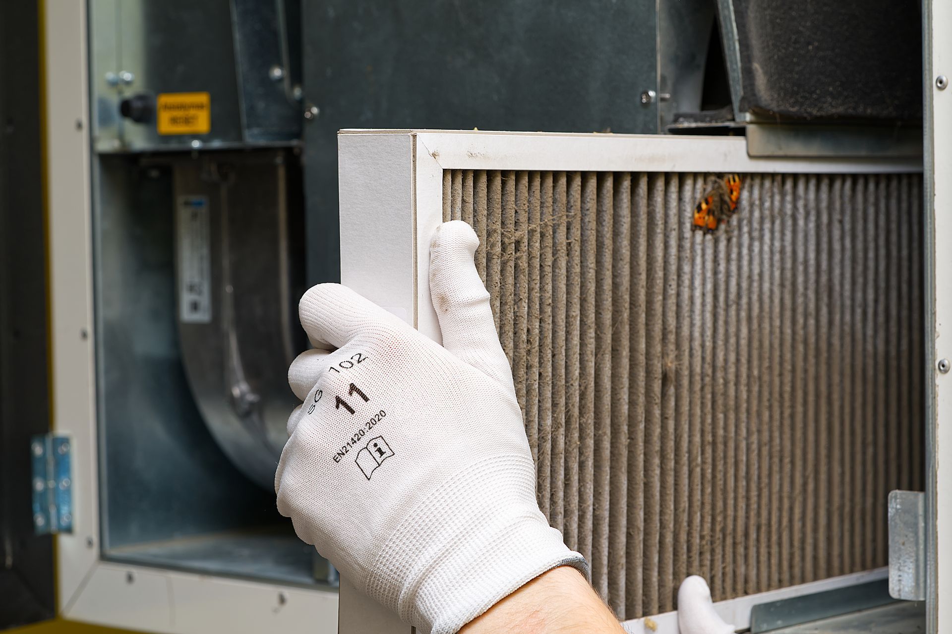 Gloved hands removing a dirty air filter from an HVAC unit.