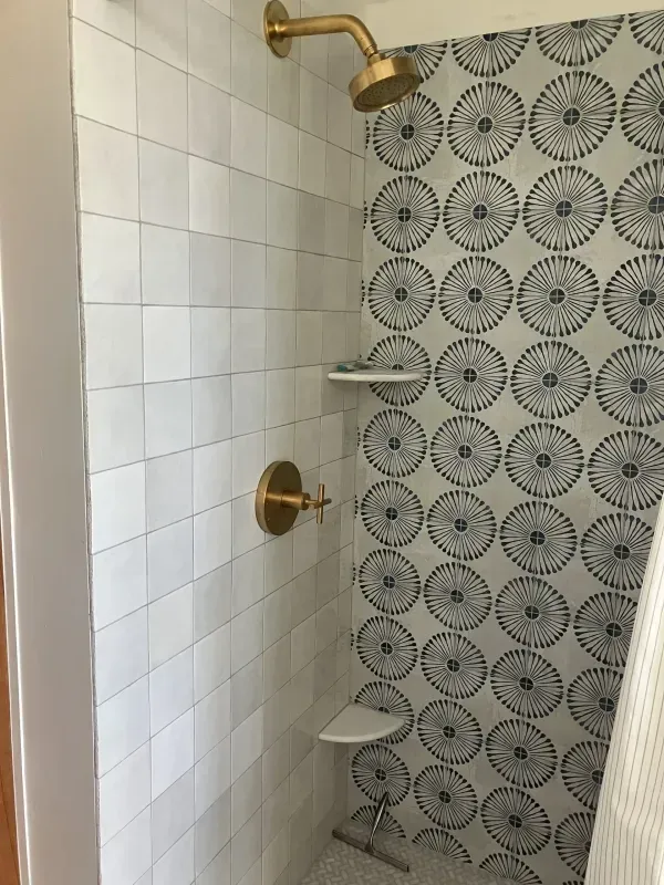 Shower with white and blue patterned tile, brass fixtures, and built-in shelves.