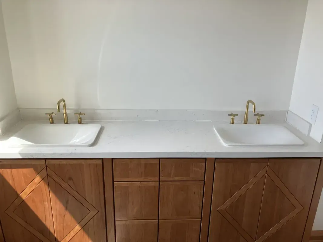 Bathroom vanity with two white sinks, gold faucets, and wood cabinets.