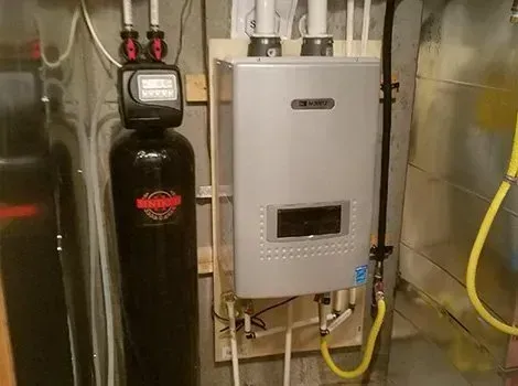 Water heater and water softener installed on a wall in a utility room. Yellow gas line.