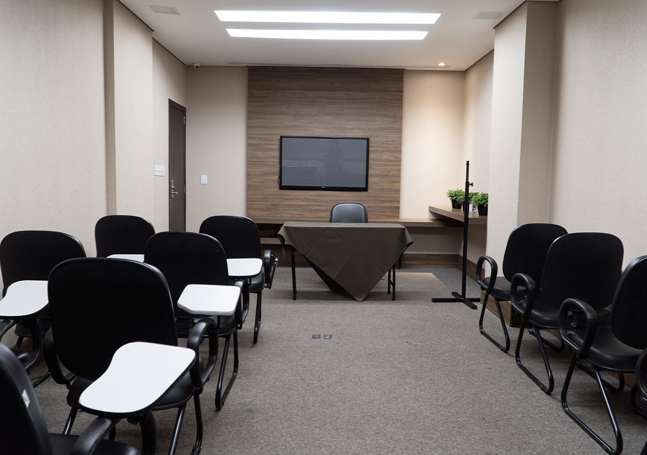 Uma sala de conferências com uma mesa e cadeiras e uma TV de tela plana na parede.