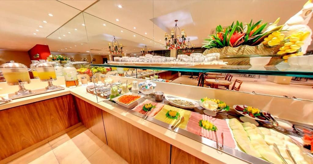 Buffet com diversas opções de exposição de alimentos, armários de madeira clara e iluminação suspensa.