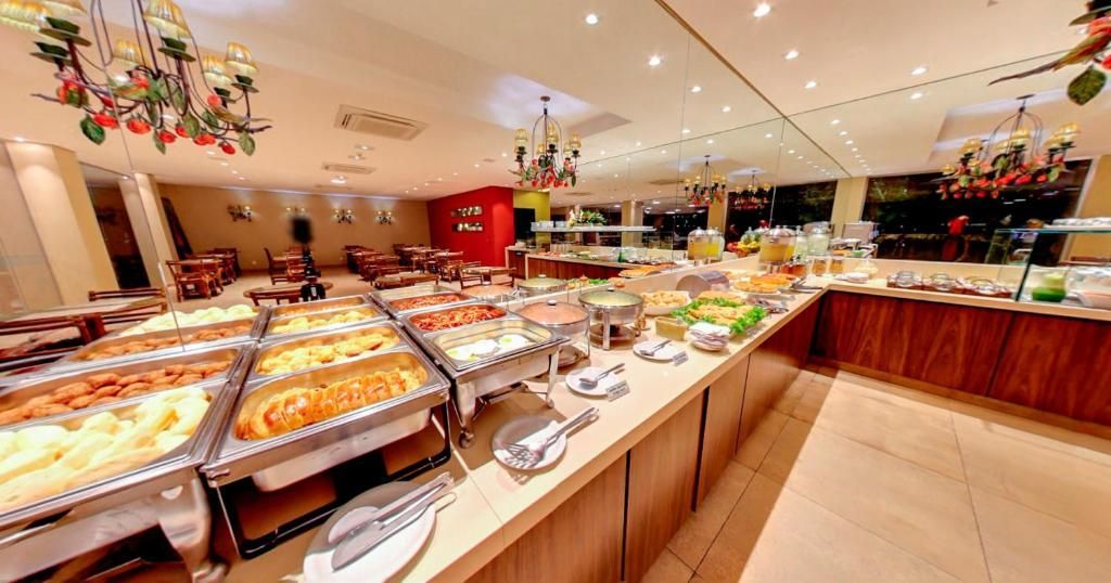 Buffet com diversas bandejas de comida, balcão de madeira, iluminação decorativa e área de estar ao fundo.