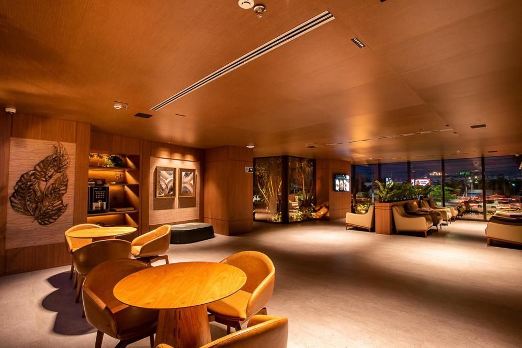 Área de estar com iluminação aconchegante, mesas redondas, cadeiras curvas.