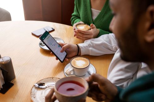 Um homem está usando um celular enquanto está sentado à mesa com duas xícaras de café.