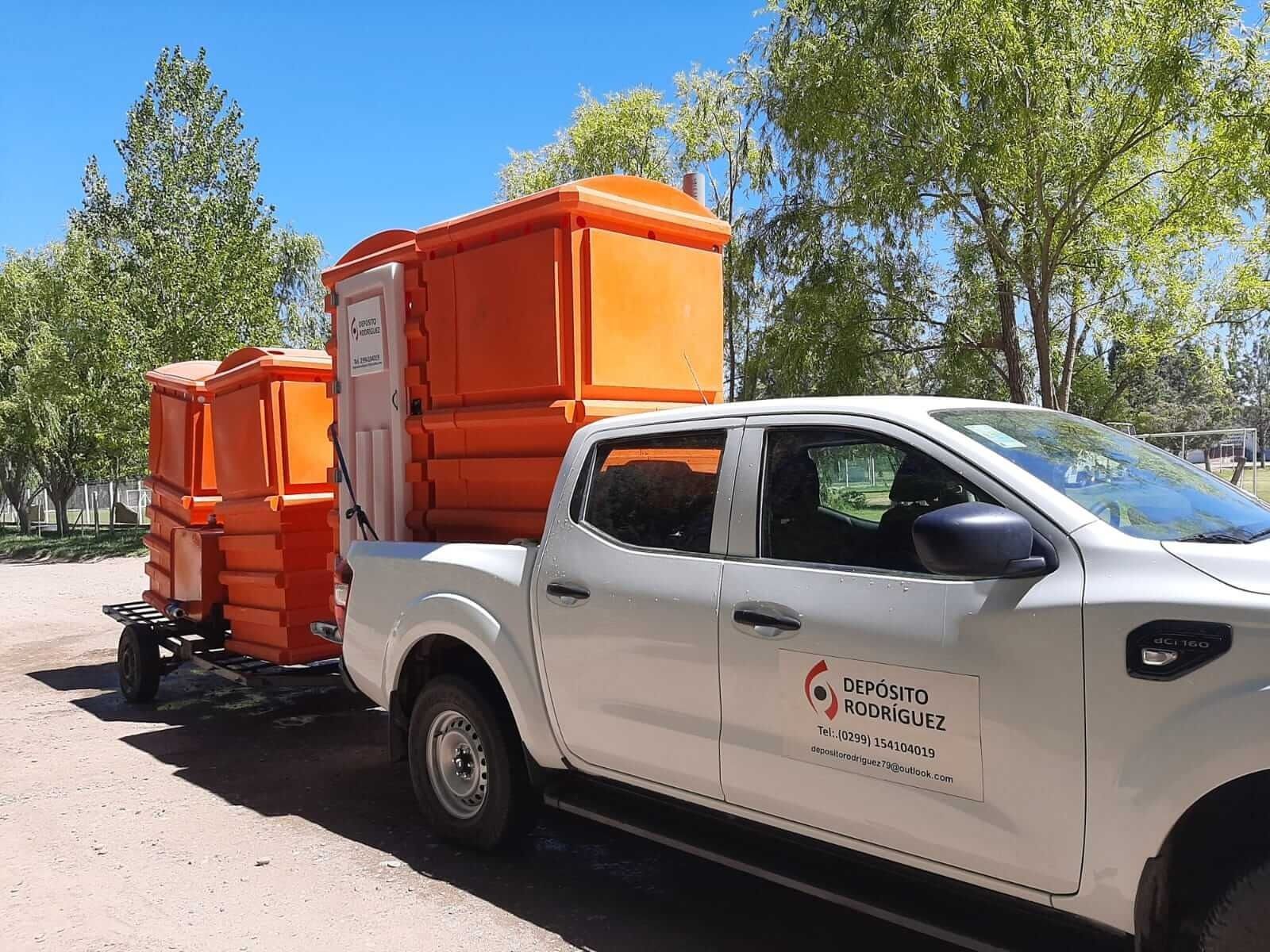Camioneta blanca transportando dos contenedores de color naranja brillante en un remolque en una zona exterior arbolada.