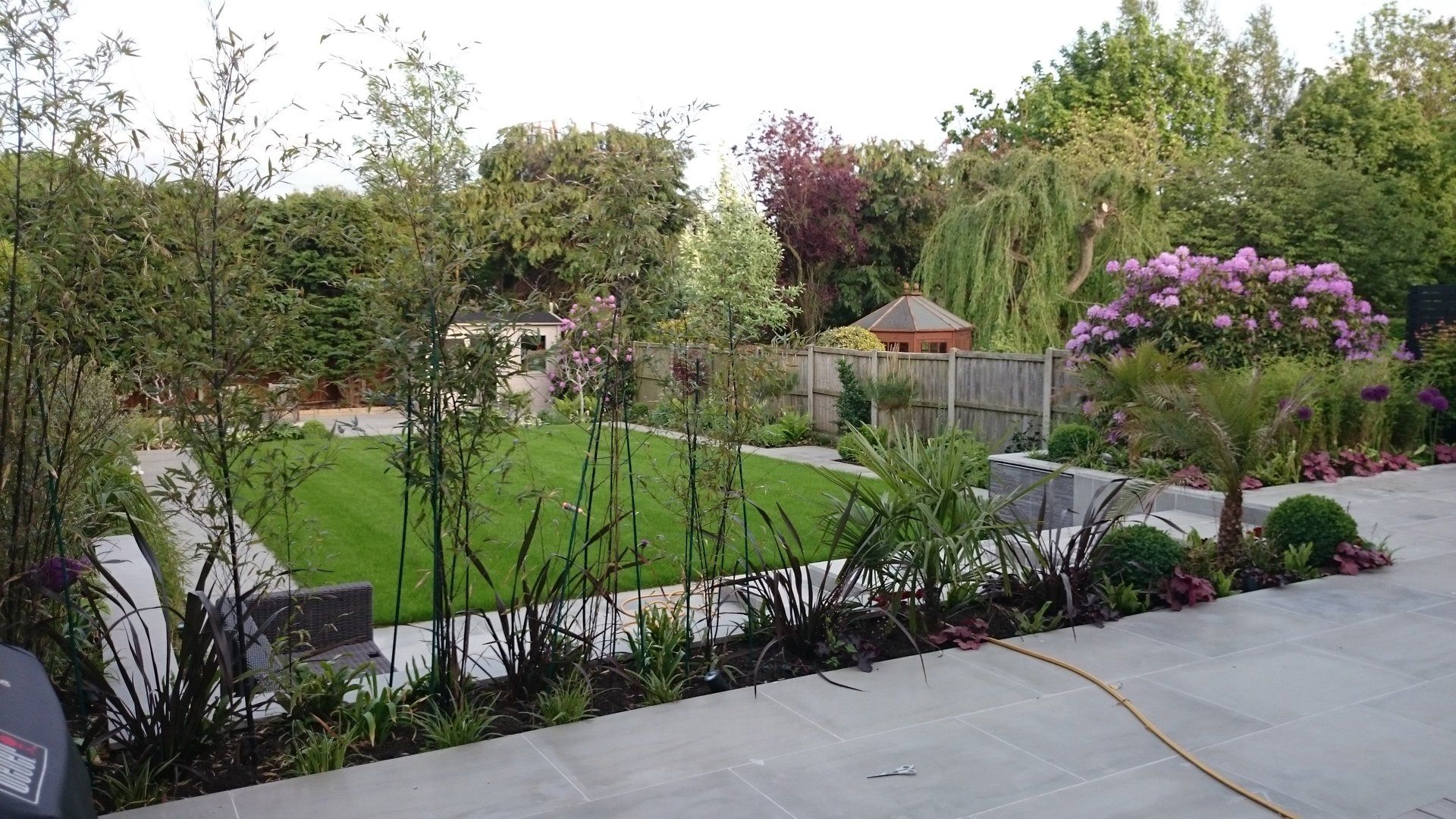 A lush green garden with a hose in the foreground and a gazebo in the background.