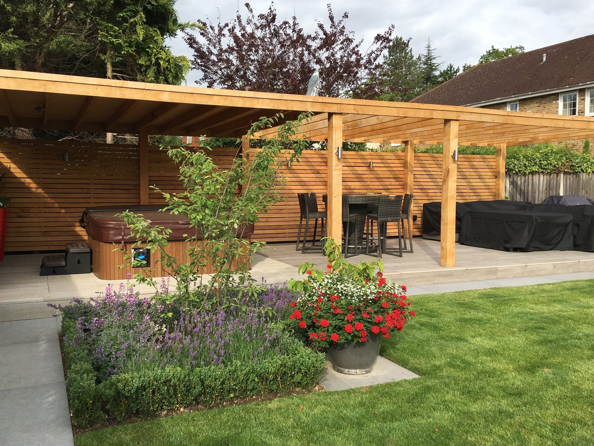 A hot tub is under a wooden pergola in a backyard.
