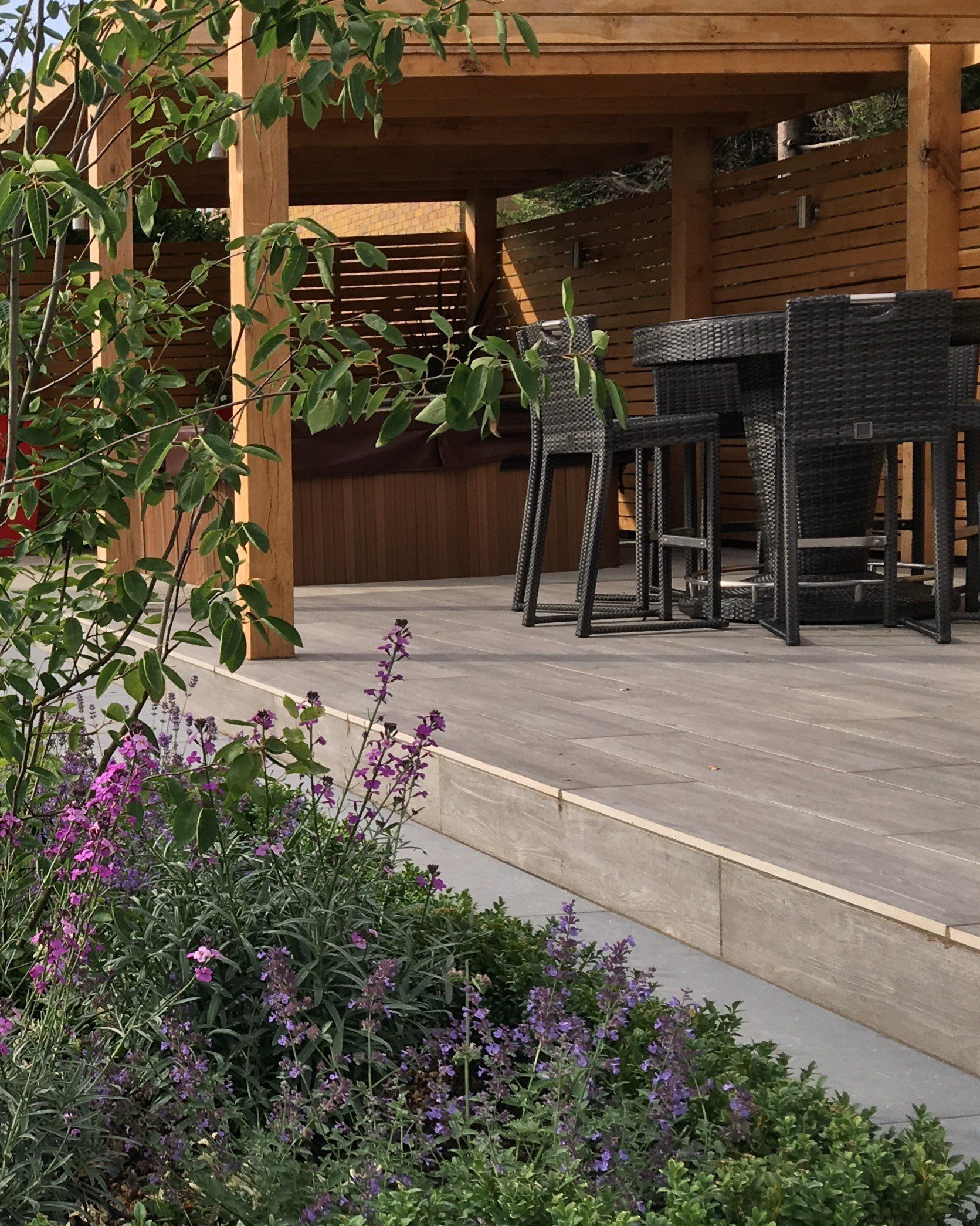 A patio with a table and chairs and purple flowers in the foreground.