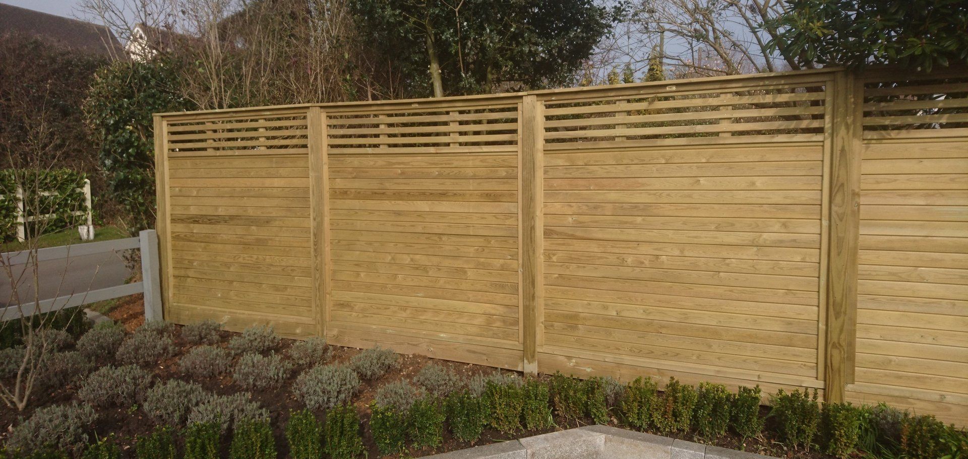 A wooden fence is surrounded by bushes and trees in a garden.