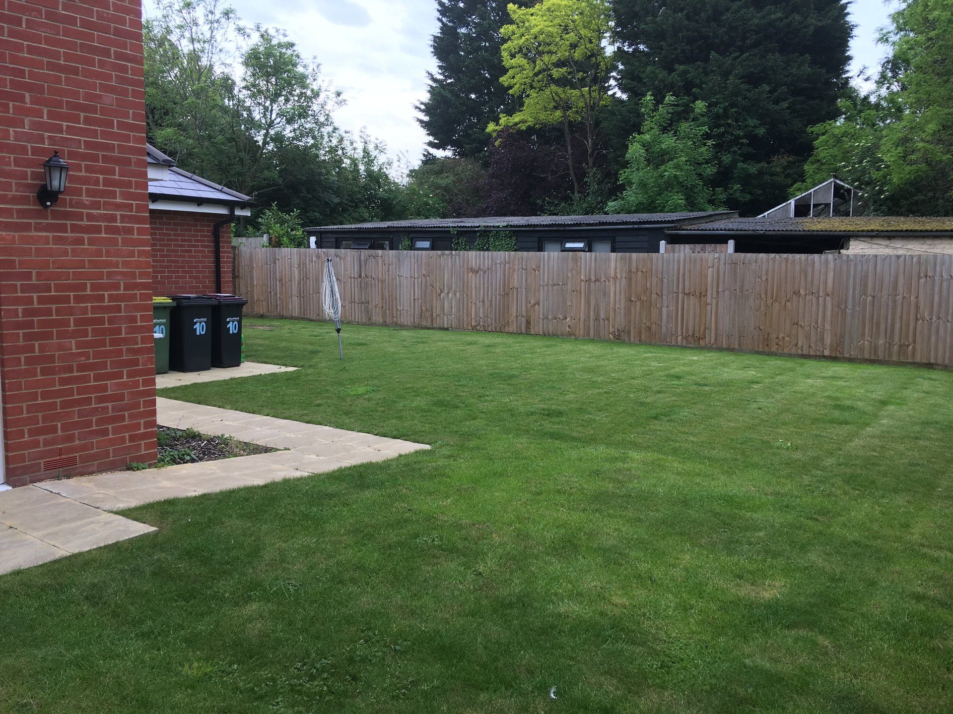 A lush green yard with a wooden fence and a brick building in the background.
