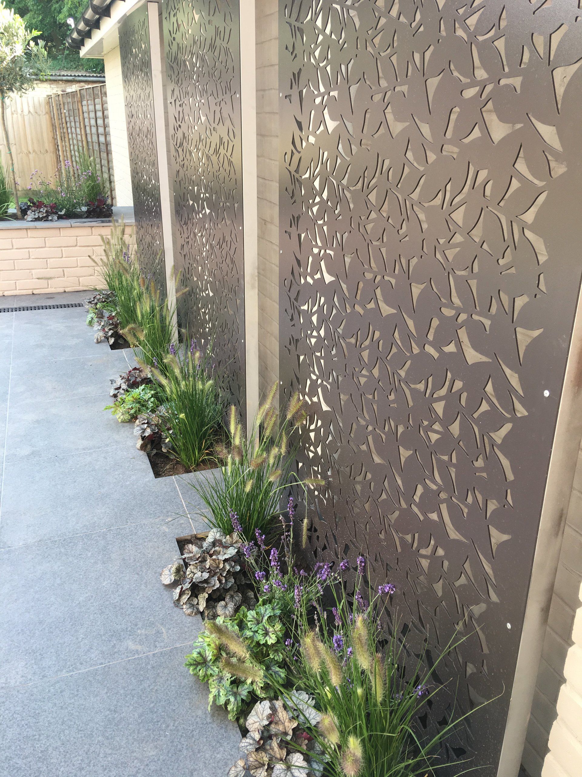A fence with a pattern on it and plants in front of it