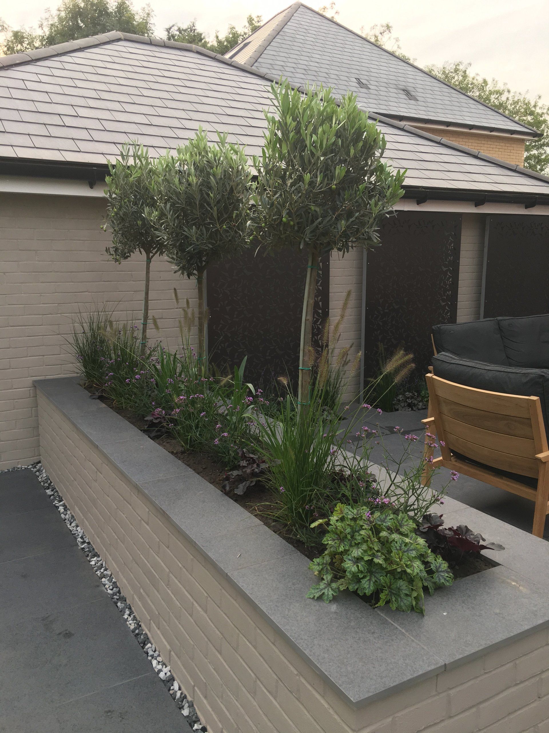 A house with a slate roof and a planter with trees in front of it.