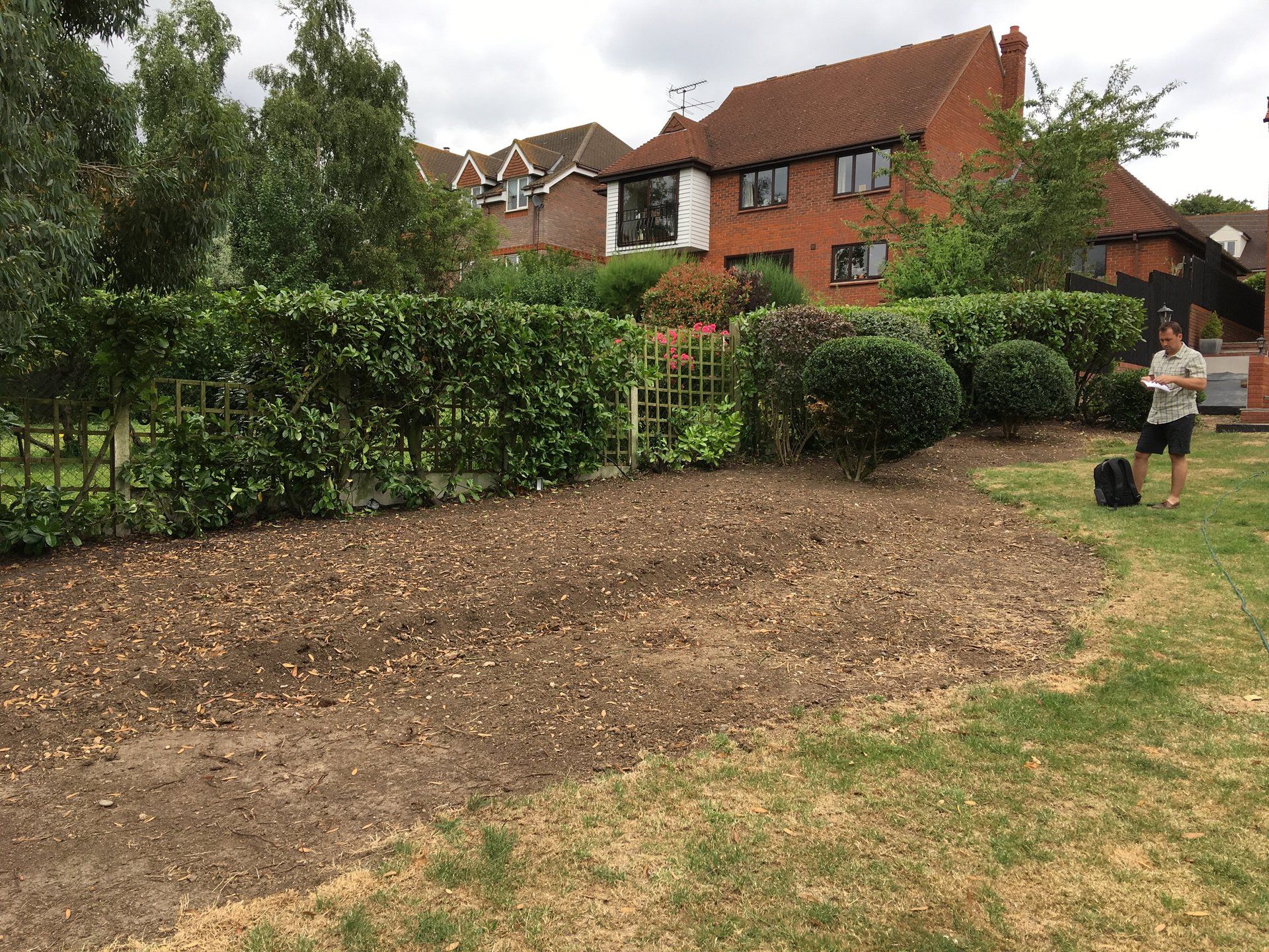 A woman is standing in a yard in front of a brick house.