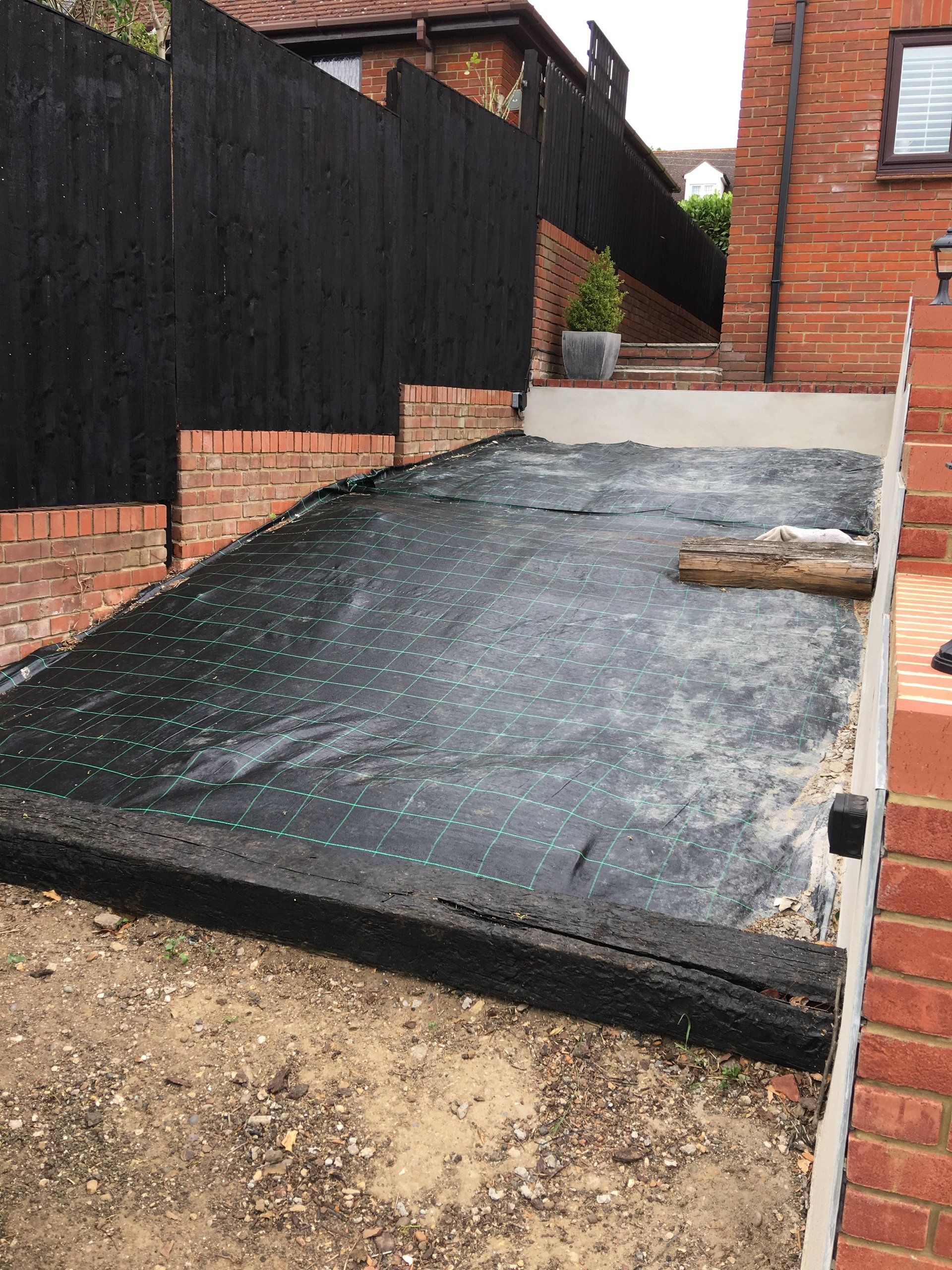 A black tarp is sitting on top of a dirt field next to a brick wall.