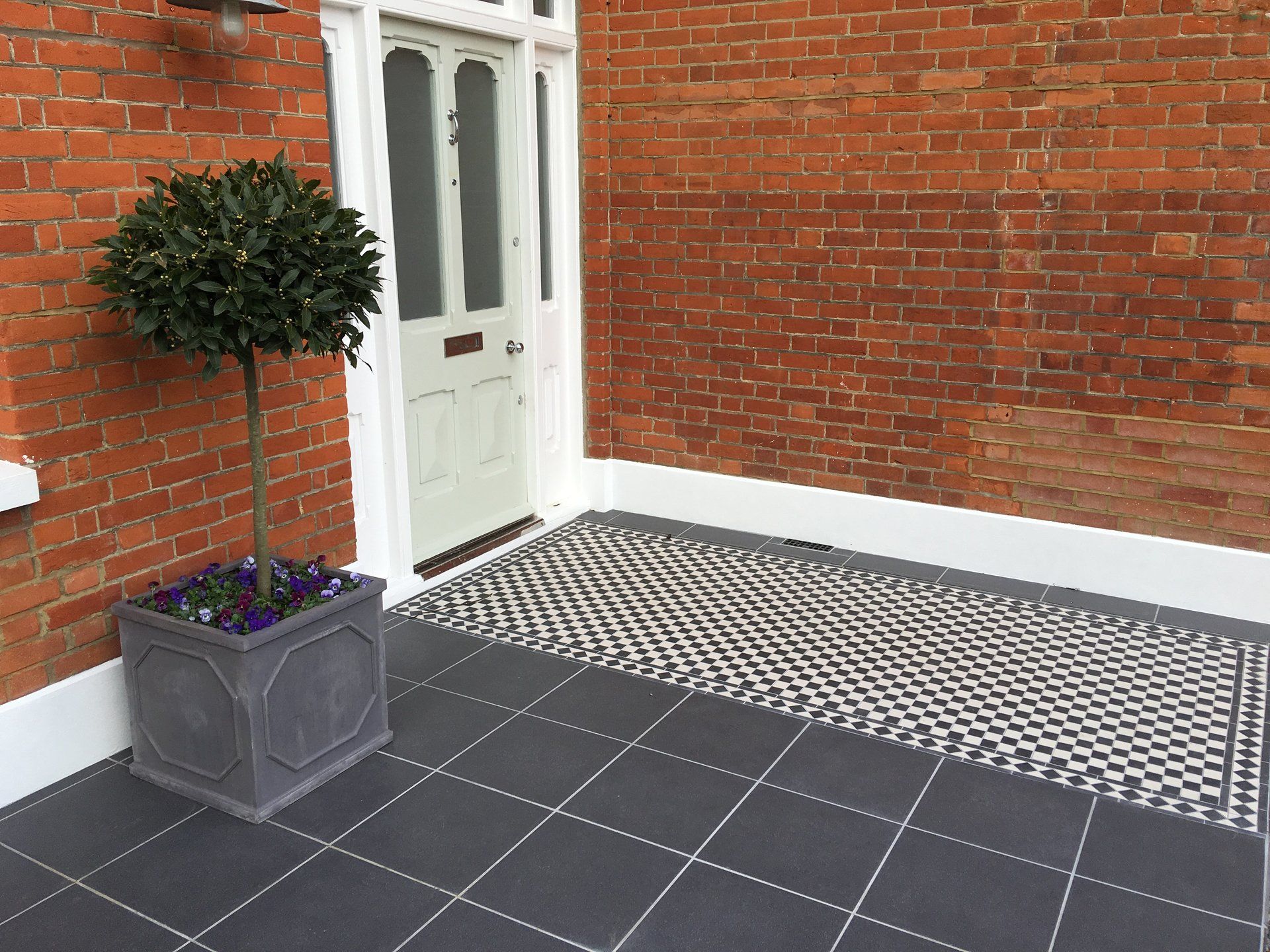 A potted plant is sitting on a tiled floor in front of a brick building.
