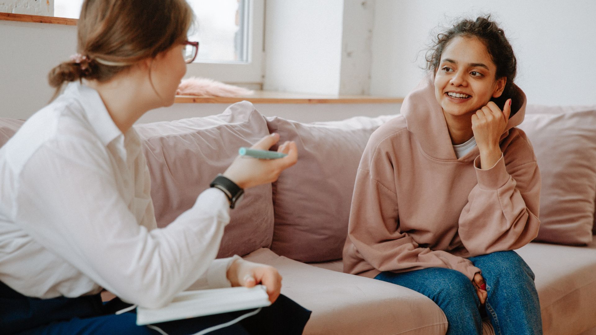 A woman is sitting on a couch talking to another woman.