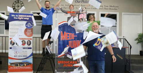 Four people smiling while throwing documents into the air in front of a 