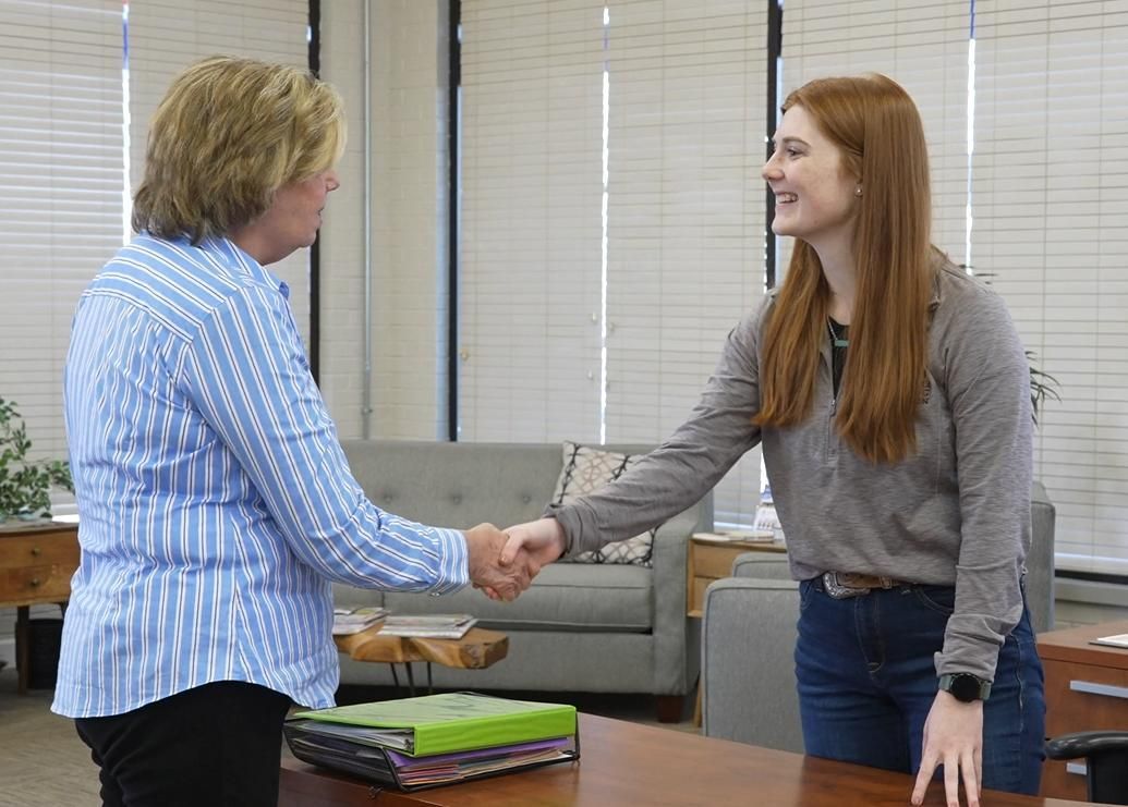 Emma greeting client with handshake in lobby.