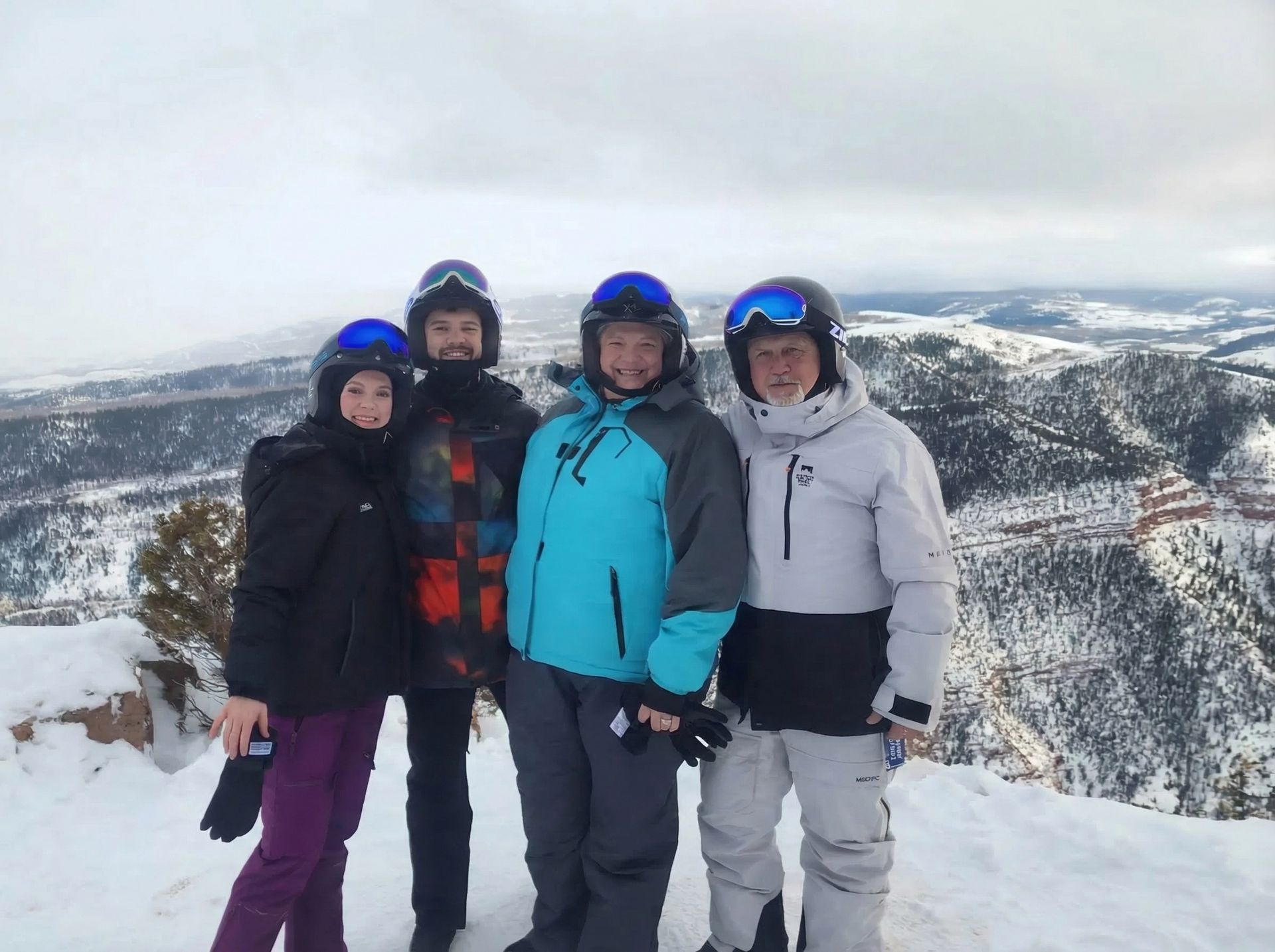 Four people in ski gear and helmets on a snow-covered mountain peak.