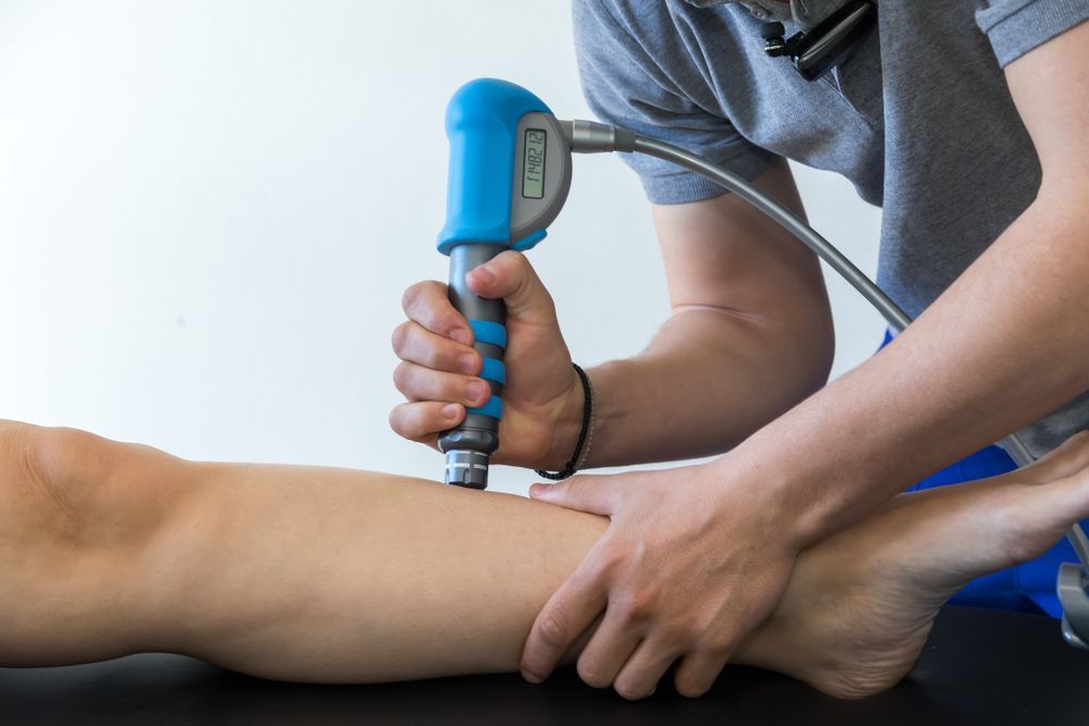 A Person Using a Blue and Gray Device on a Patient's Lower Leg — Biomedical Sports Podiatry in Forster, NSW