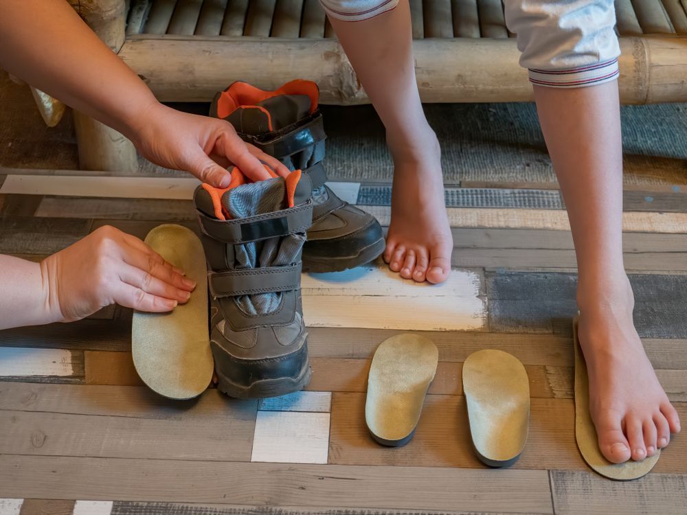 Person's Feet Next to Insoles and a Boot — Biomedical Sports Podiatry in Forster, NSW