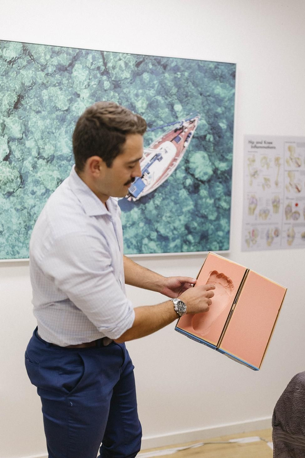 A Man is Holding a Piece of Paper in Front of a Painting of a Boat in the Ocean— Biomedical Sports Podiatry in Forster, NSW