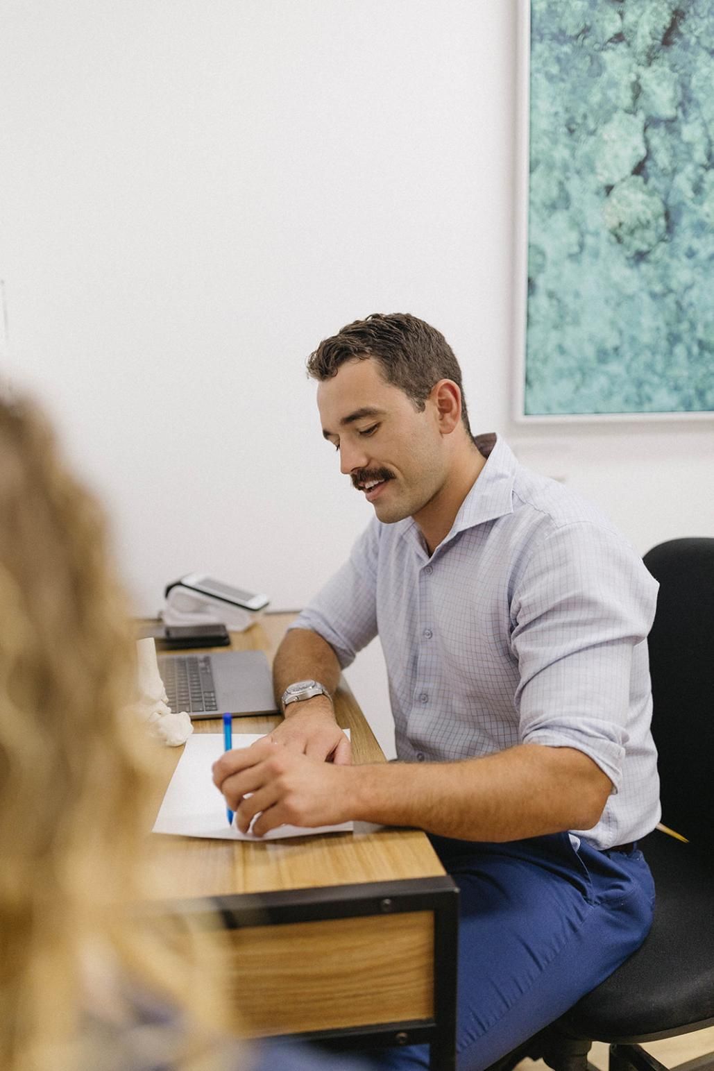 A Man is Sitting at a Desk Writing on a Piece of Paper — Biomedical Sports Podiatry in Gloucester, NSW