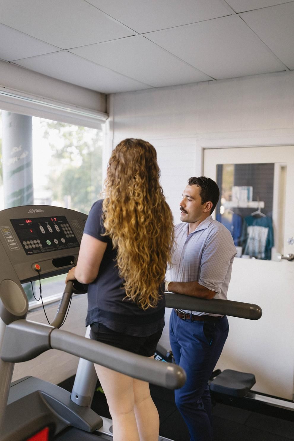 A Man is Helping a Woman on a Treadmill in a Gym — Biomedical Sports Podiatry in Gloucester, NSW