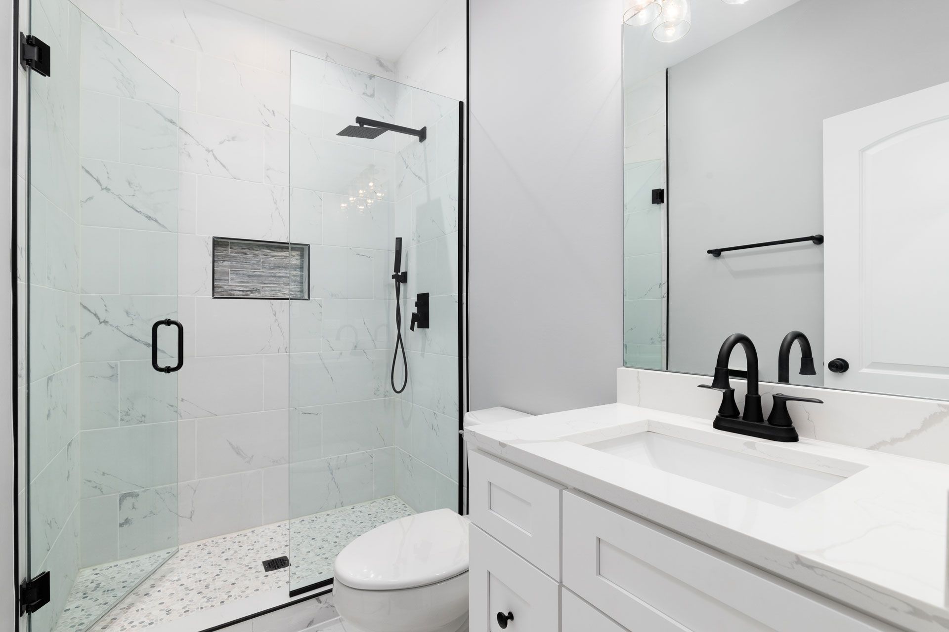 Modern bathroom with marble tile shower, black fixtures, and white vanity.