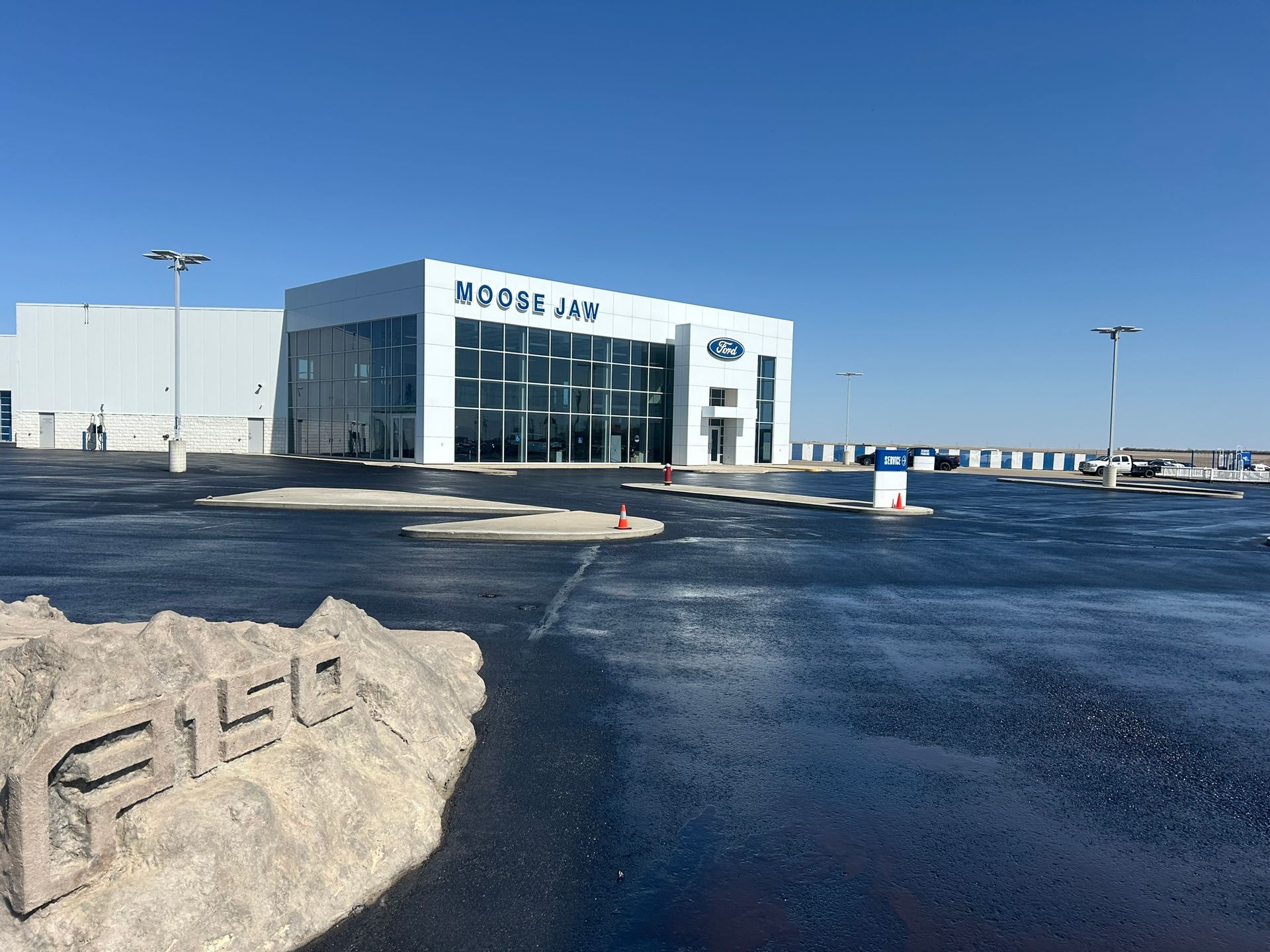 Woman in straw hat smiles, holding wine glass near a lake.