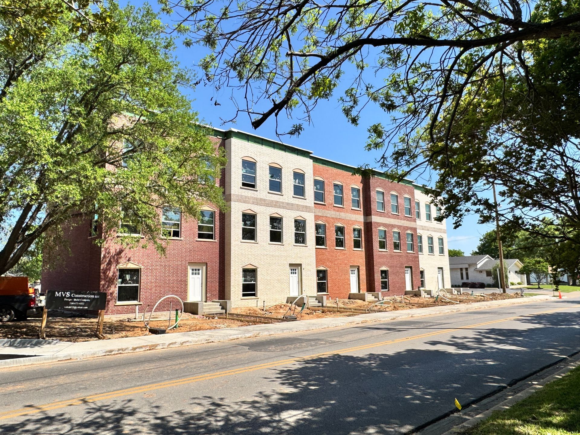 Row of multi-story townhouses under construction; various brick colors, blue sky, tree in foreground.
