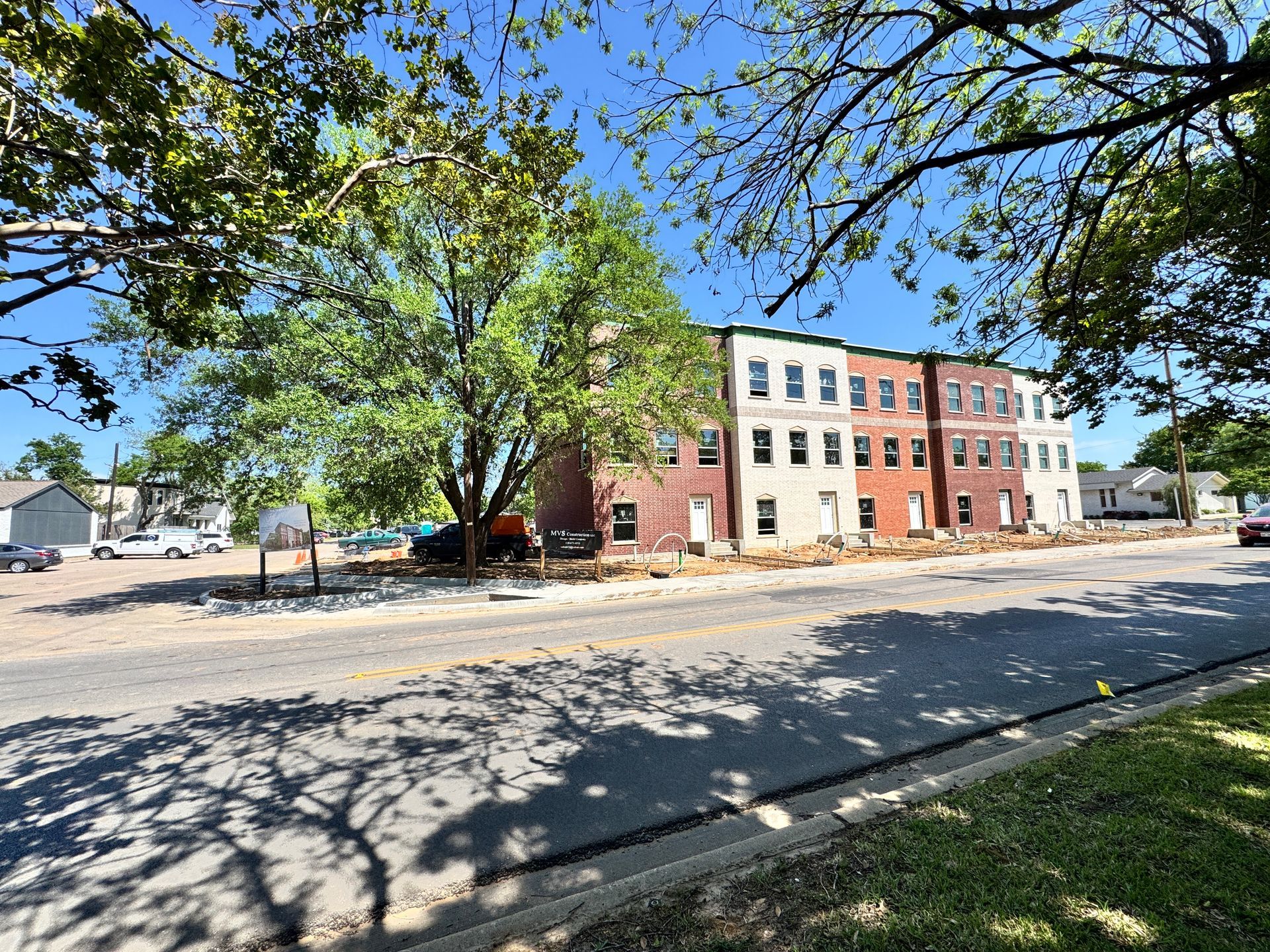 Three-story brick apartment building under construction next to a tree, viewed from across the street on a sunny day.