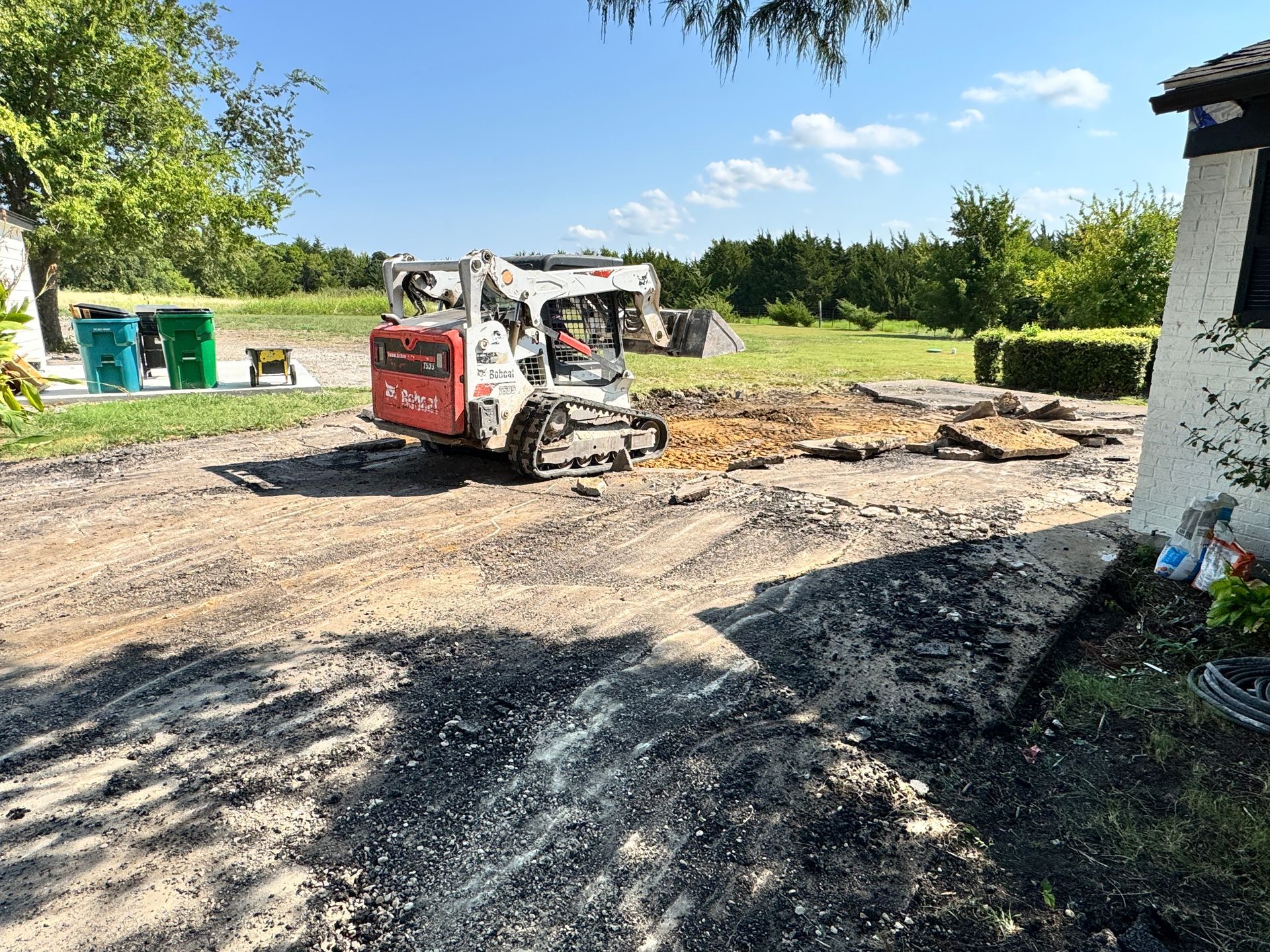 Bobcat construction vehicle on a dirt surface, next to a house under a bright blue sky.