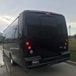 The back of a black bus is parked on the side of the road.