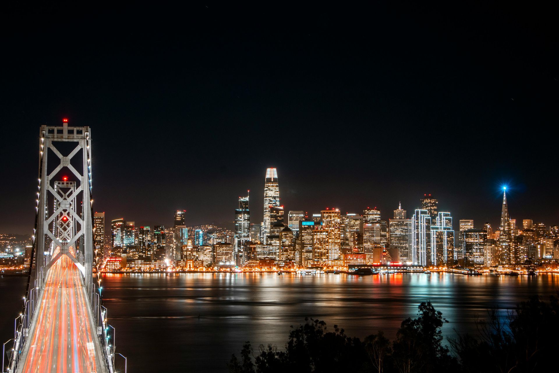 A bridge over a body of water with a city skyline in the background at night.