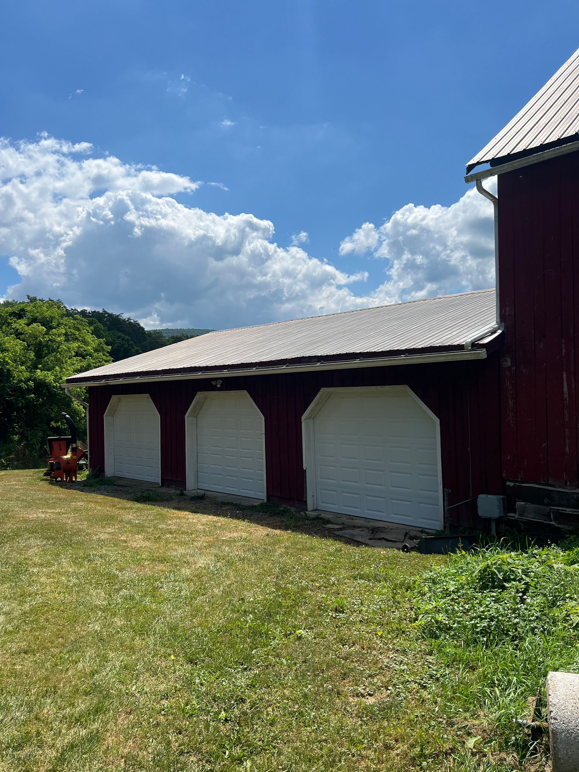 A red barn with white garage doors is sitting in the middle of a grassy field.