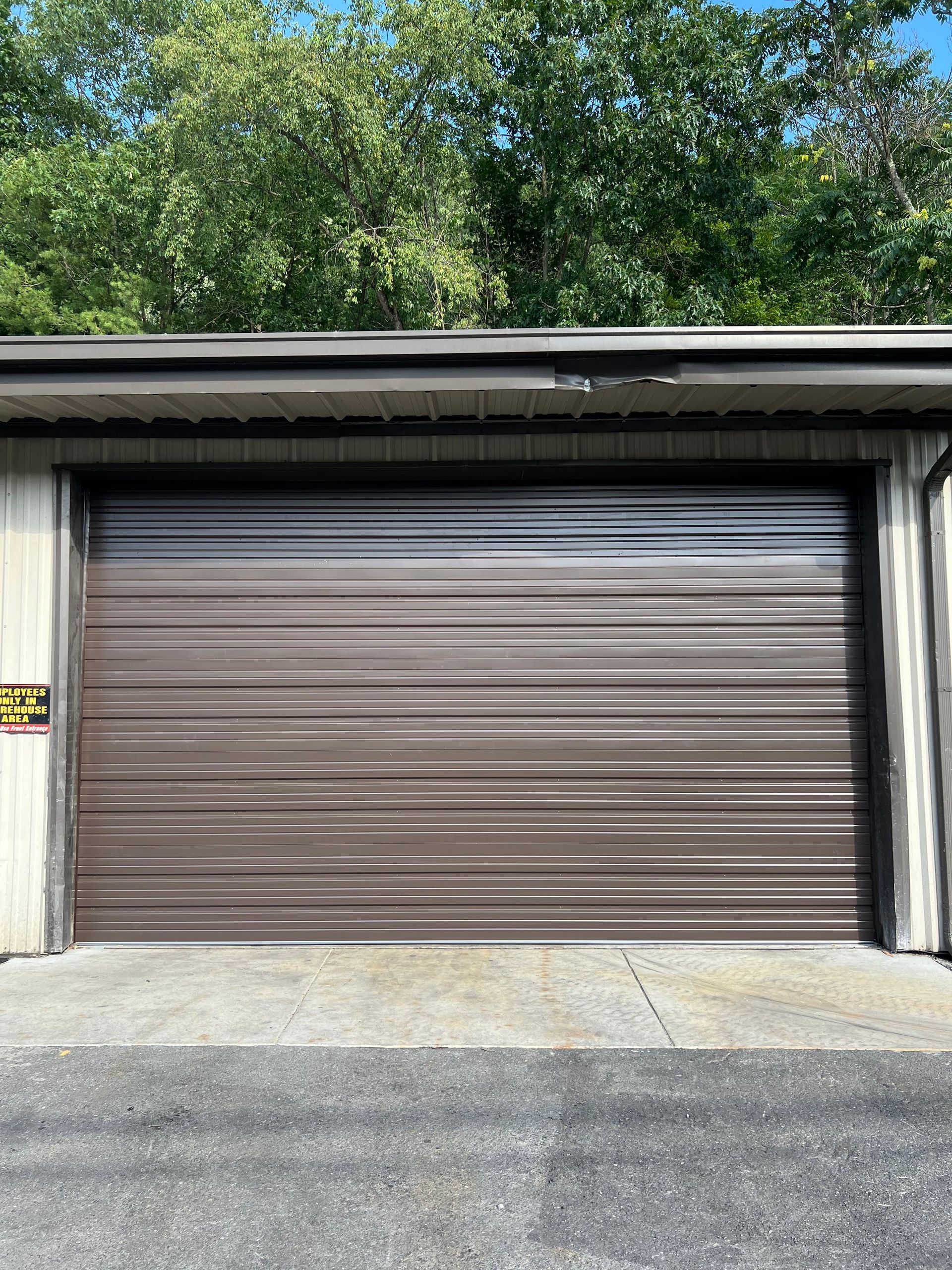 A brown garage door is sitting in front of a building with trees in the background.