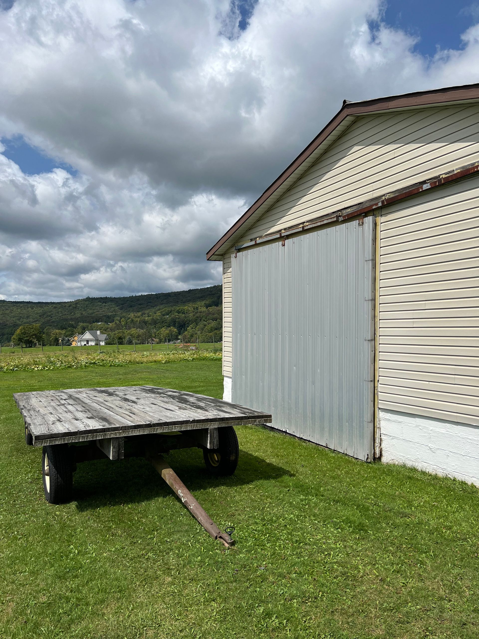 A wooden trailer is parked in a grassy field next to a building.